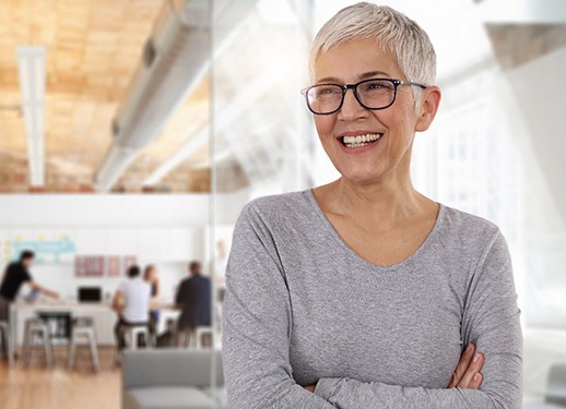 Woman in grey shirt smiling with arms crossed while indoors