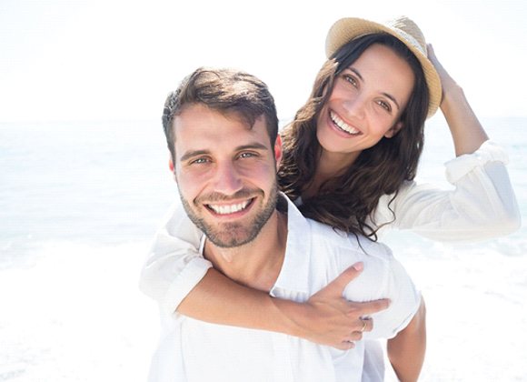 young couple wearing white and smiling on the beach