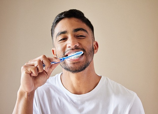 Man in white shirt smiling while brushing his teeth