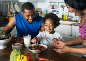 a child smiling and eating healthy foods with her mom and dad