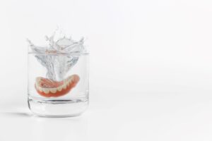 Set of dentures splashing into a glass of liquid with a white background